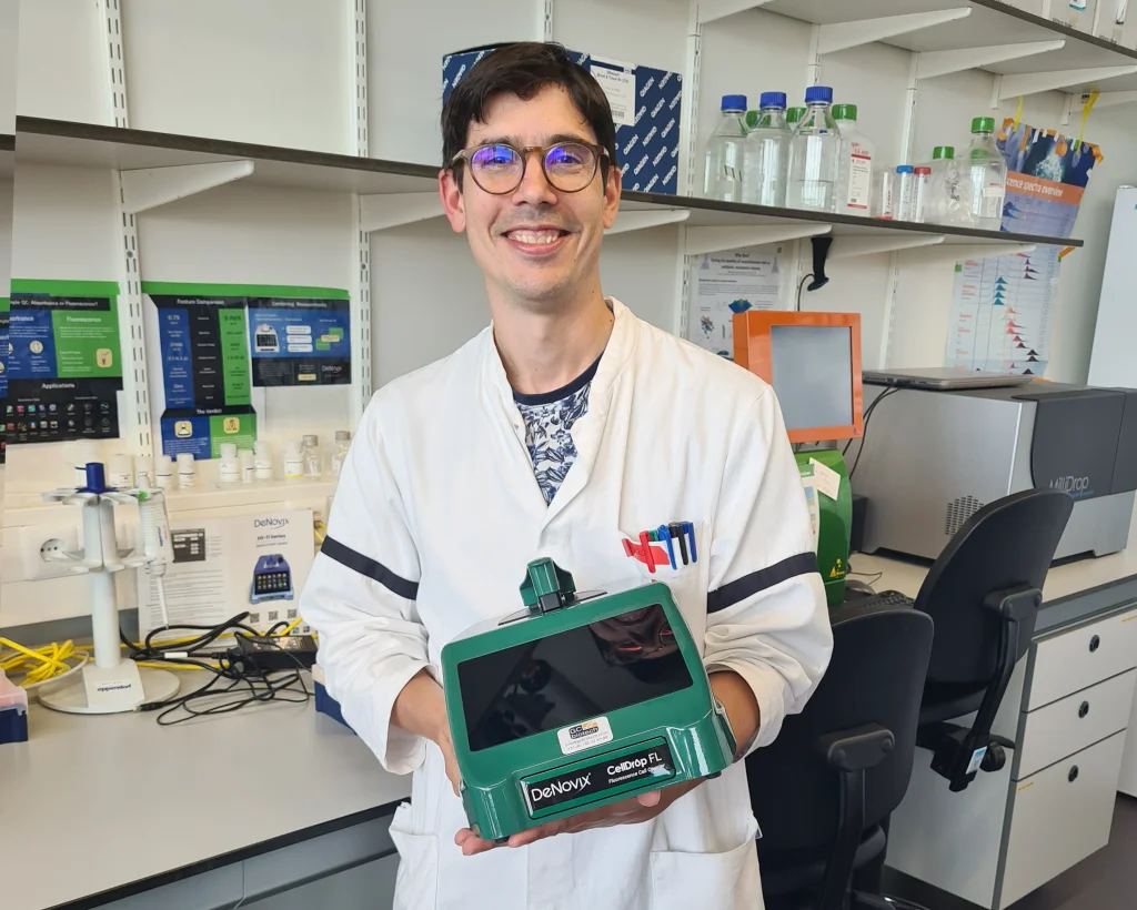 smiling scientist holding green celldrop with shelving in background